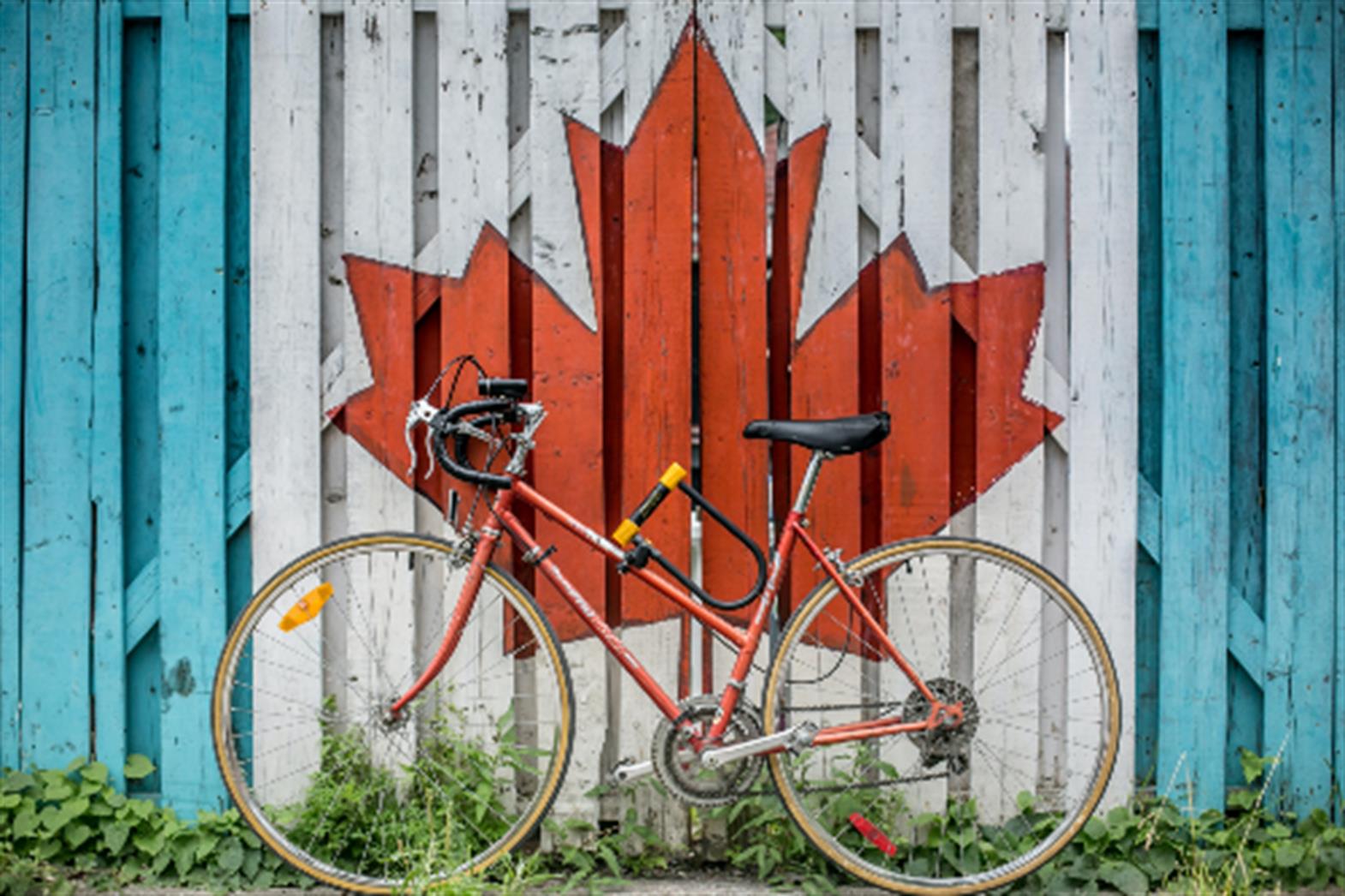 a red bicycle leaning against a fence. The fence has a maple leaf painted on it. 