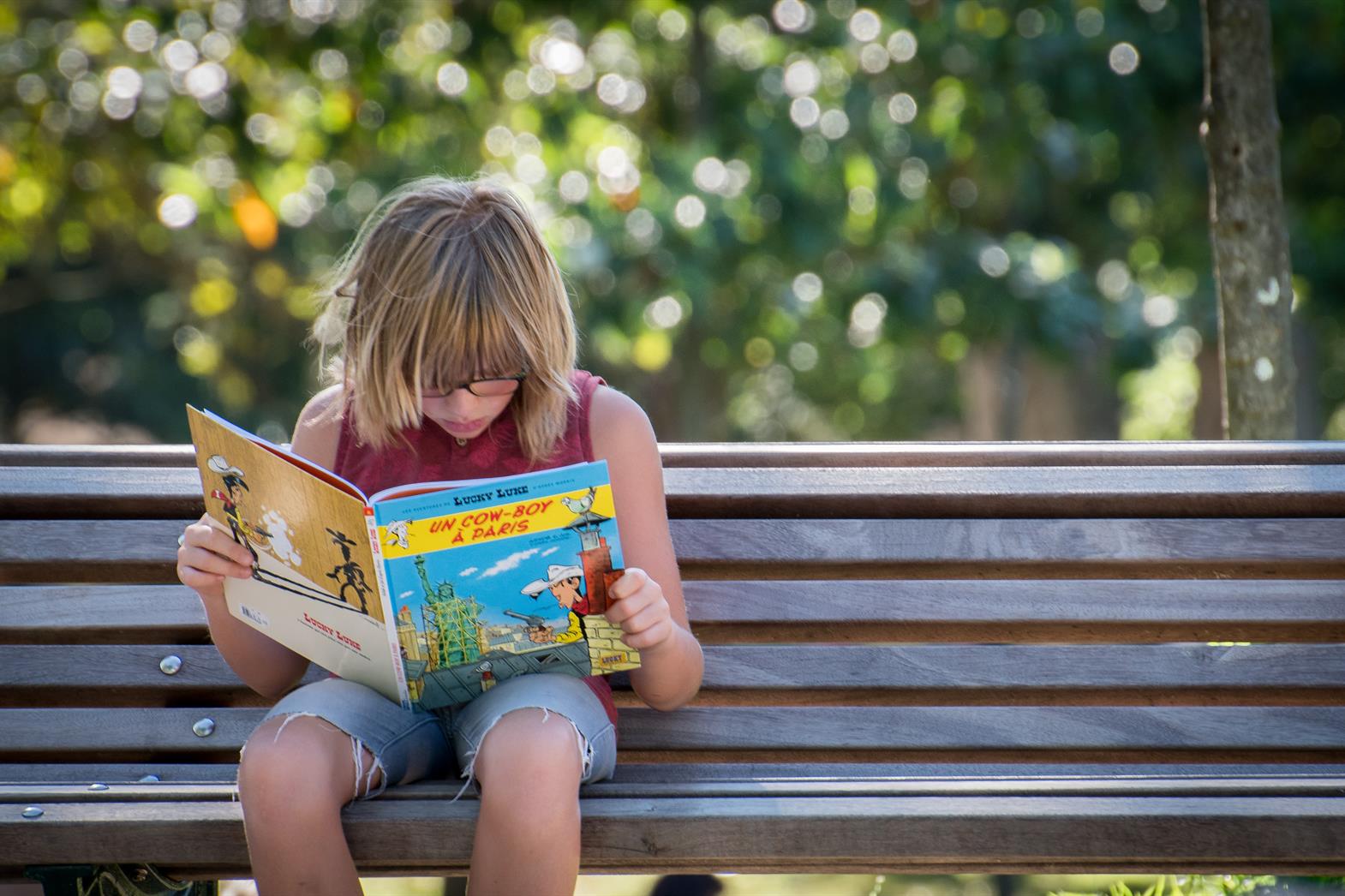 Child about 13 years old sitting on a bench reading a children's book