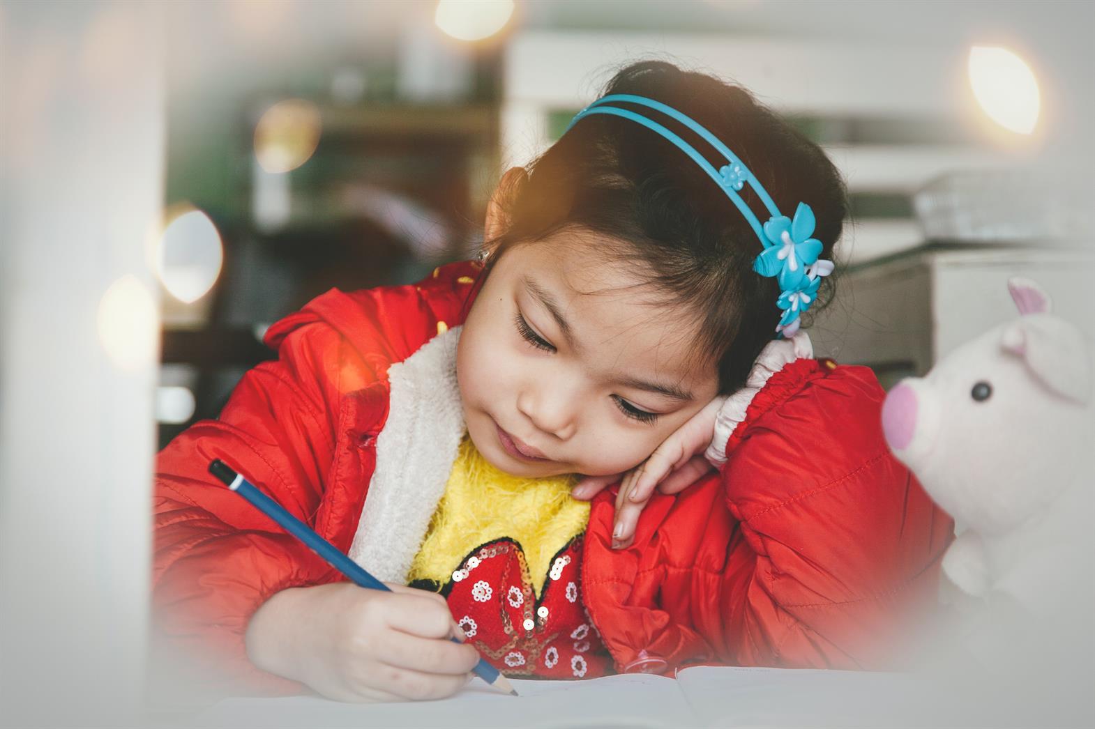 Young girl writing with a pencil in a workbook