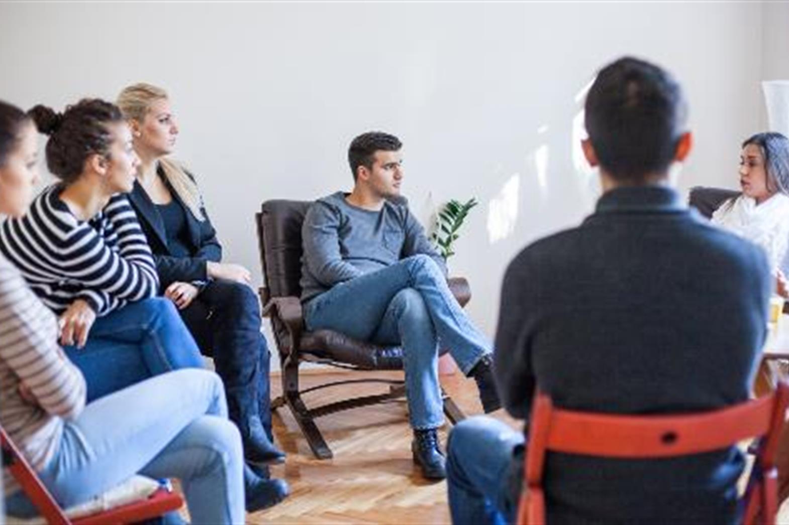 a multicultural group of people sitting in a circle on chairs, talking