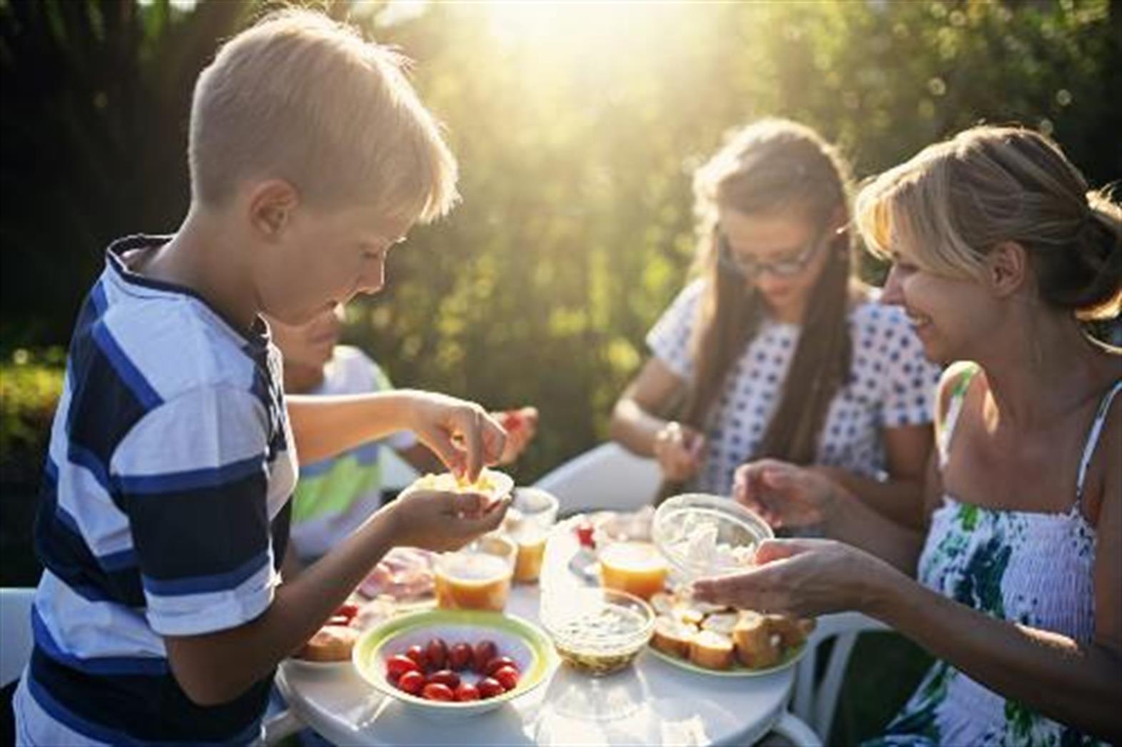 several people around a picnic table selecting food to eat and smiling