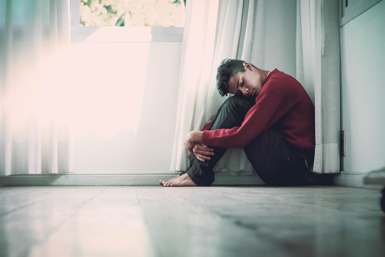 A young man sitting on the floor with his head on his knees