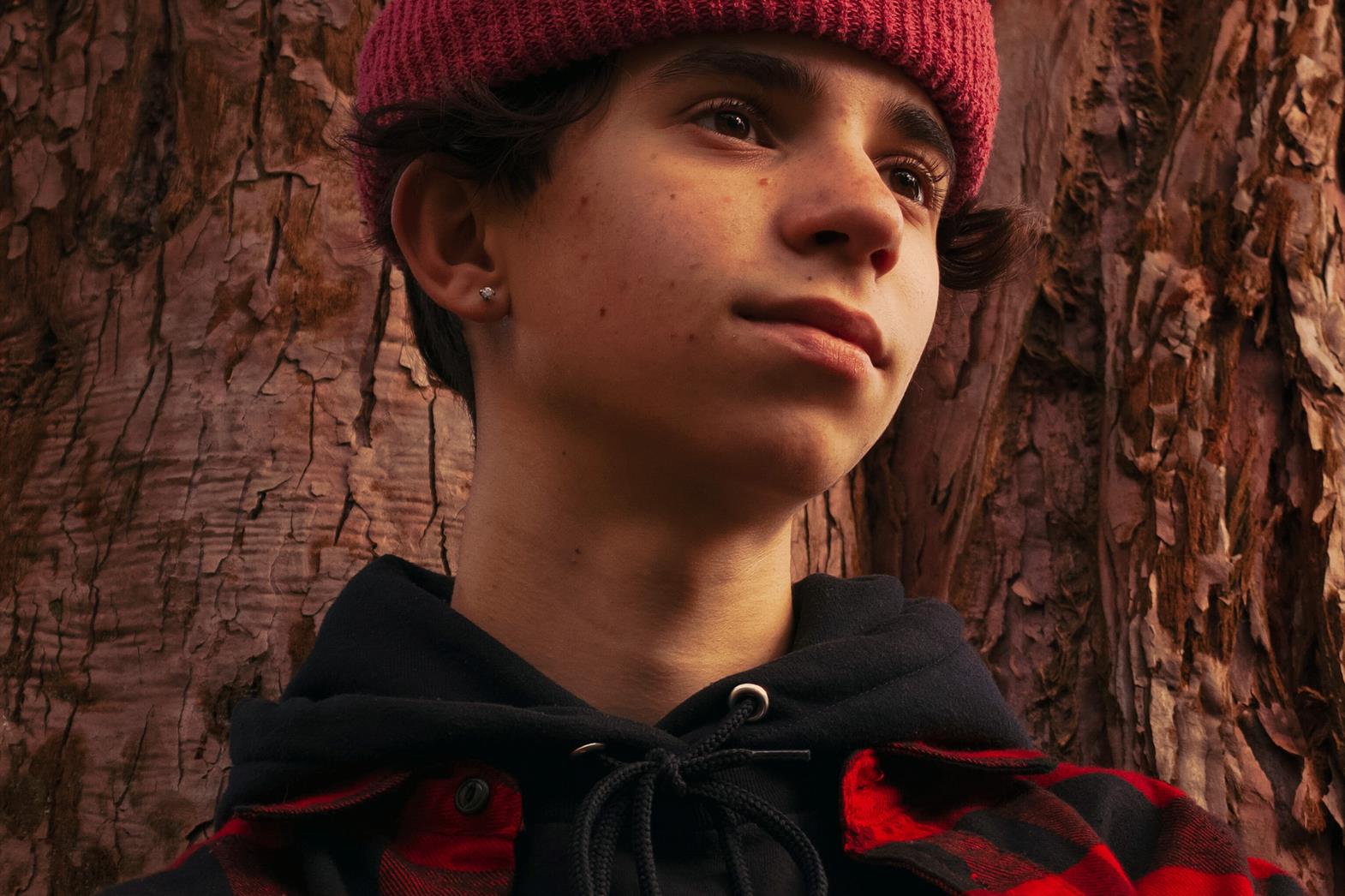 A young person wearing plaid and a toque looks off camera