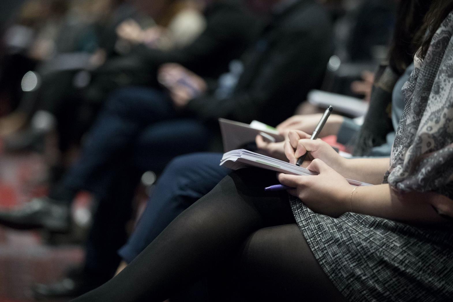 Woman sitting in a chair writing in a notebook on her lap.