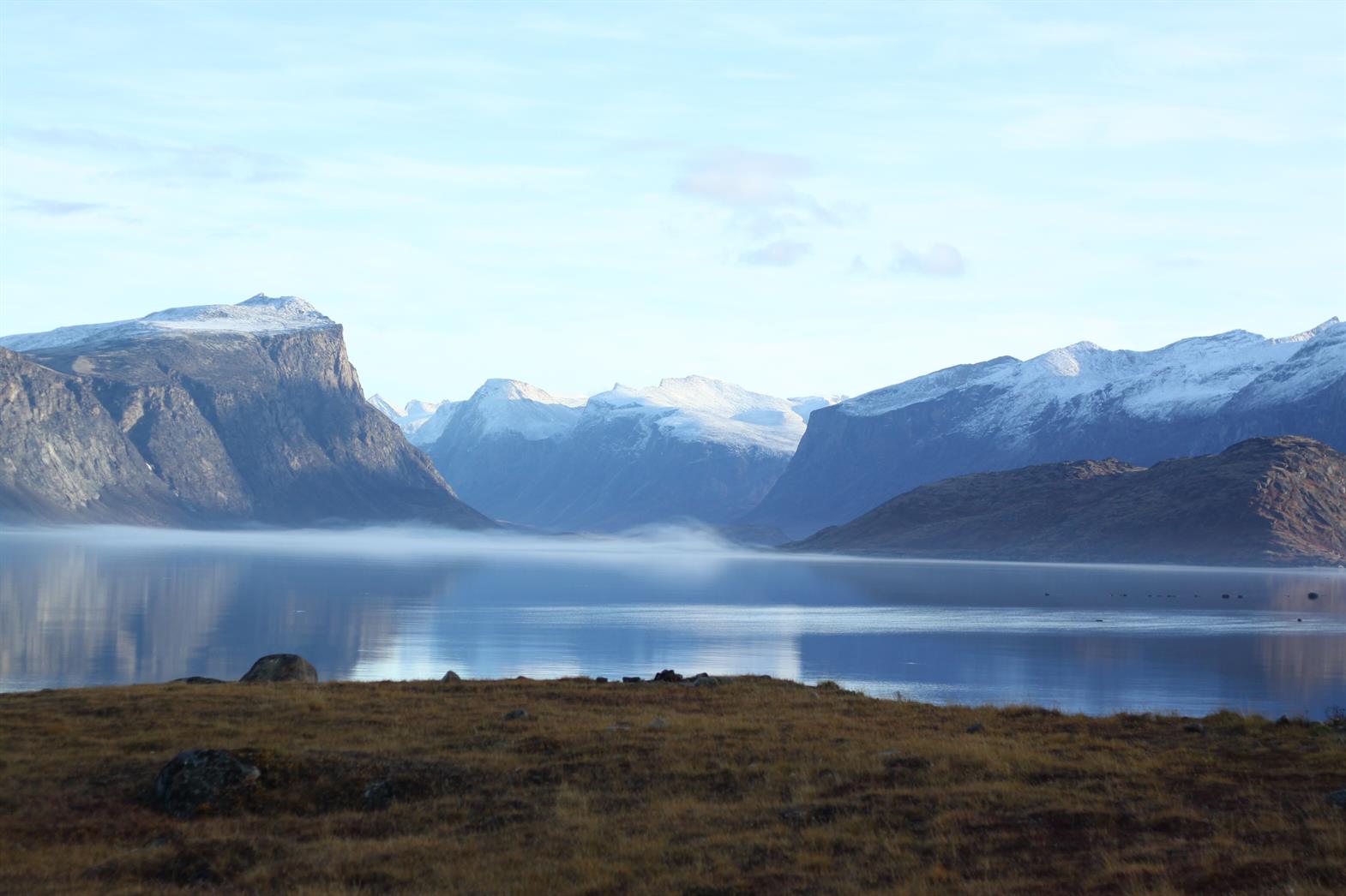 tundra and a blue lake with snow capped mountains in the distance