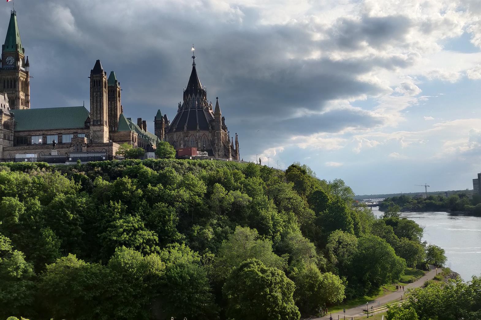 The Ottawa parliament buildings and beside the river. Green trees in the foreground.